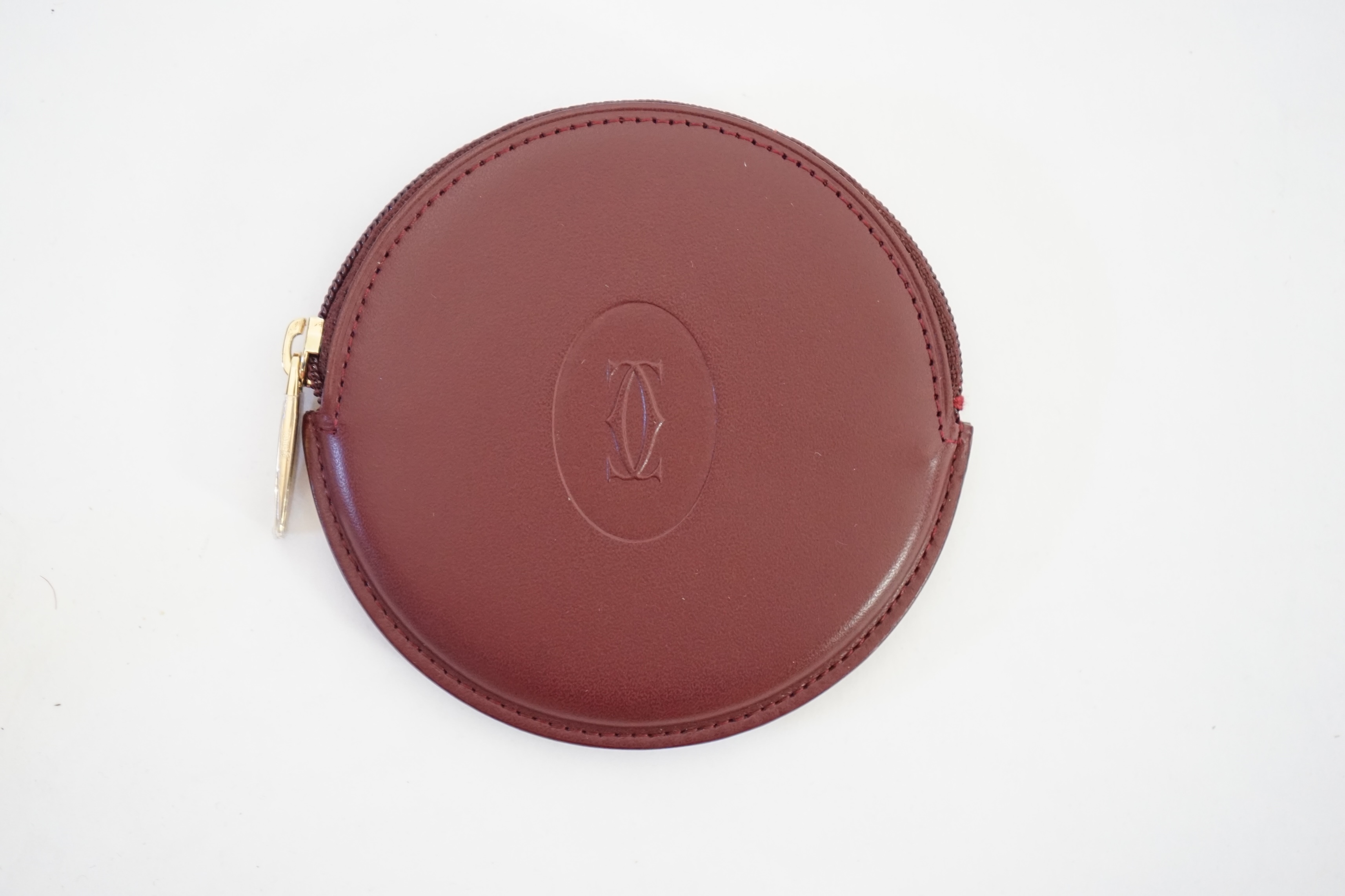 A Cartier maroon leather circular purse with box.